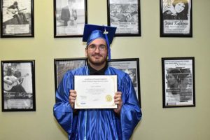 Graduate in blue cap and gown holding diploma