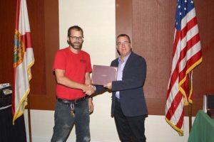 Two men shaking hands with certificate near flags