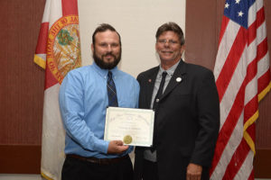 Two men holding award certificate by flags