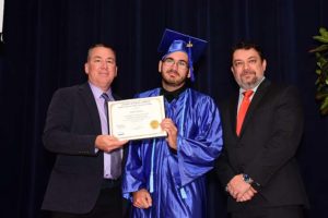 Graduate in blue cap and gown holding diploma