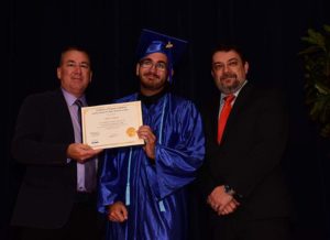 Graduate in blue gown holding diploma with men.