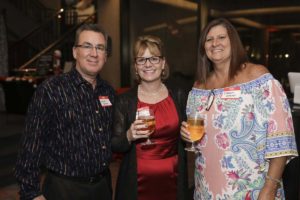 Three adults smiling, holding wine glasses