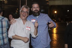 Two men smiling, one holding wine glass