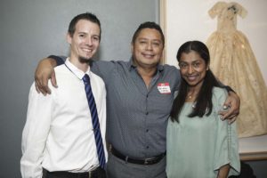 Three people smiling with arms around shoulders