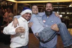 Three men at party, one wears Santa hat