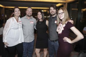 Five smiling adults posing at indoor event