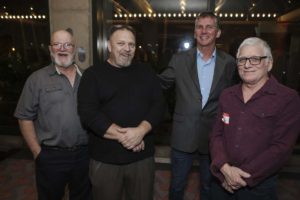 Four men smiling and posing indoors