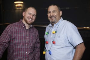 Two men smiling, one wearing colorful light necklace