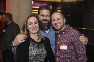 Three smiling adults posing at an indoor event