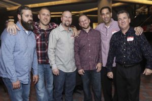Group of six men smiling at social event
