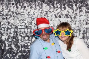Two adults wearing oversized holiday glasses, silver backdrop