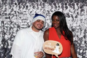 Smiling couple in festive photo booth with sign