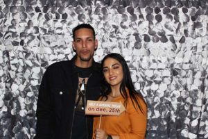 Two adults holding holiday sign, silver sequin backdrop