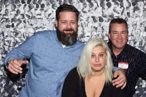 Three adults posing with wine glass at backdrop