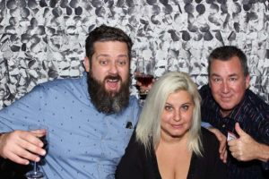 Three adults posing with drinks in photo booth