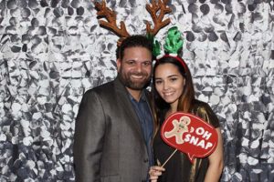 Smiling couple wearing reindeer antlers holding holiday sign