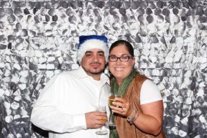 Smiling people holding drinks, wearing blue Santa hat