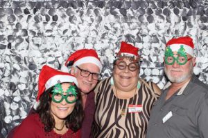 Four adults wearing Santa hats and novelty glasses