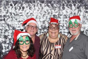 Four adults wearing Santa hats and festive glasses