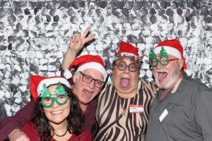 Four adults in Santa hats with Christmas glasses