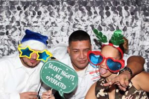Three people with oversized holiday glasses and sign