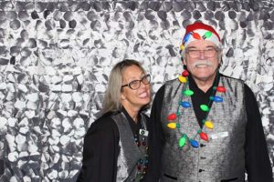 Two people wearing holiday lights, silver backdrop