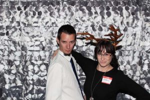 Two people posing, one wearing antler headband