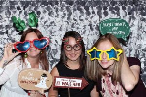 Three women in festive glasses holding holiday signs