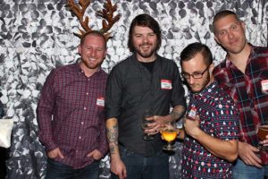Four men posing with drinks, one wearing antlers