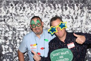 Two men in festive glasses holding a sign