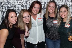 Five women smiling together at a social event