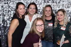 Five women smiling at party with backdrop