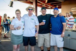 Four adults posing with drinks at outdoor event