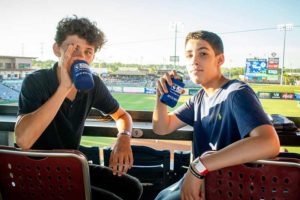 Two teens at baseball game holding drinks