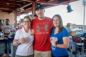 Three friends smiling at a ballpark with drinks