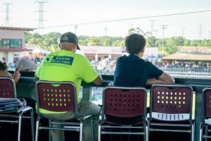 Two men seated at railing watching outdoor event